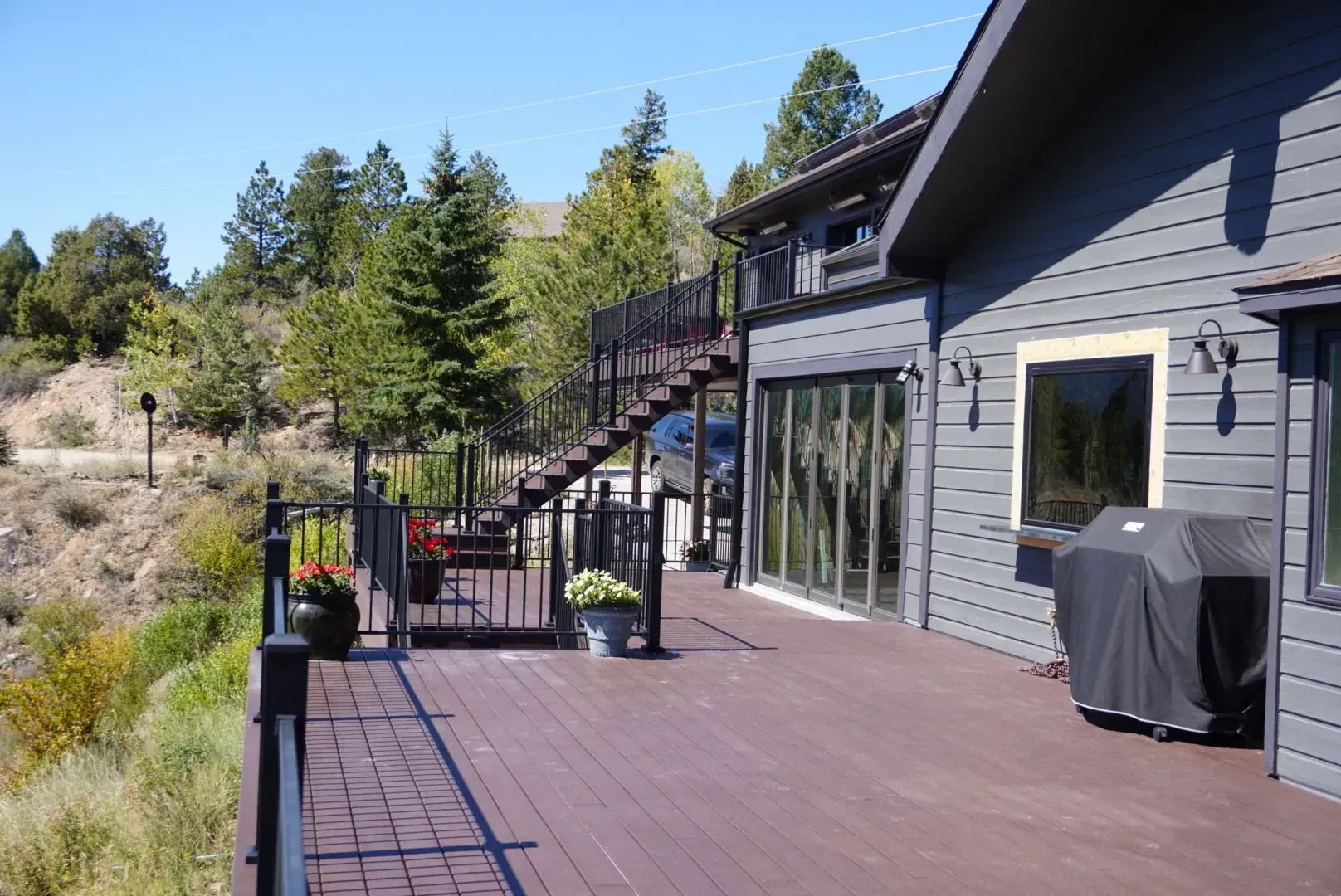 Deck with stairs, house exterior, and grill. Trees and a hillside in the background.