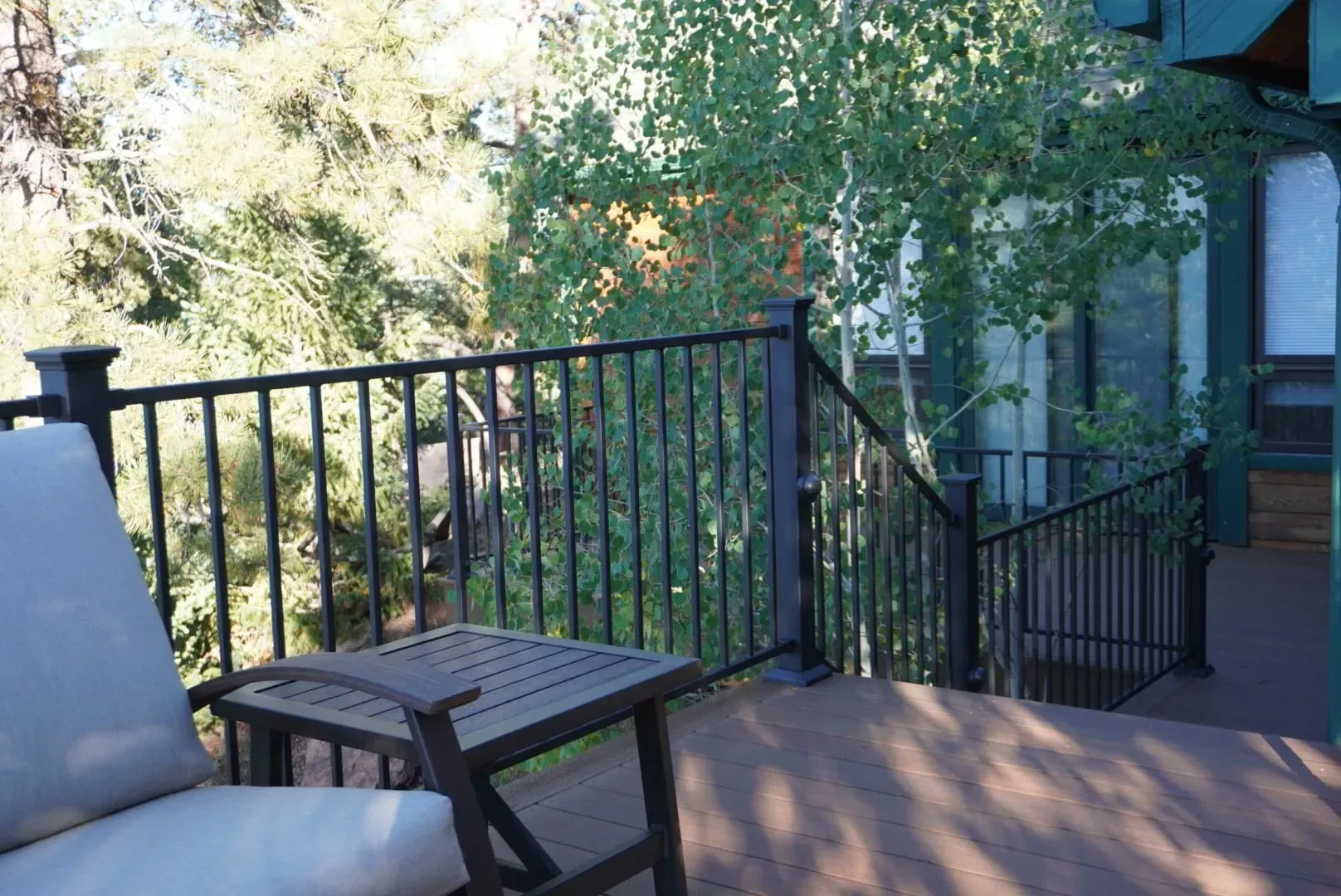 Wooden deck with black railing, table, and chair; trees in background.