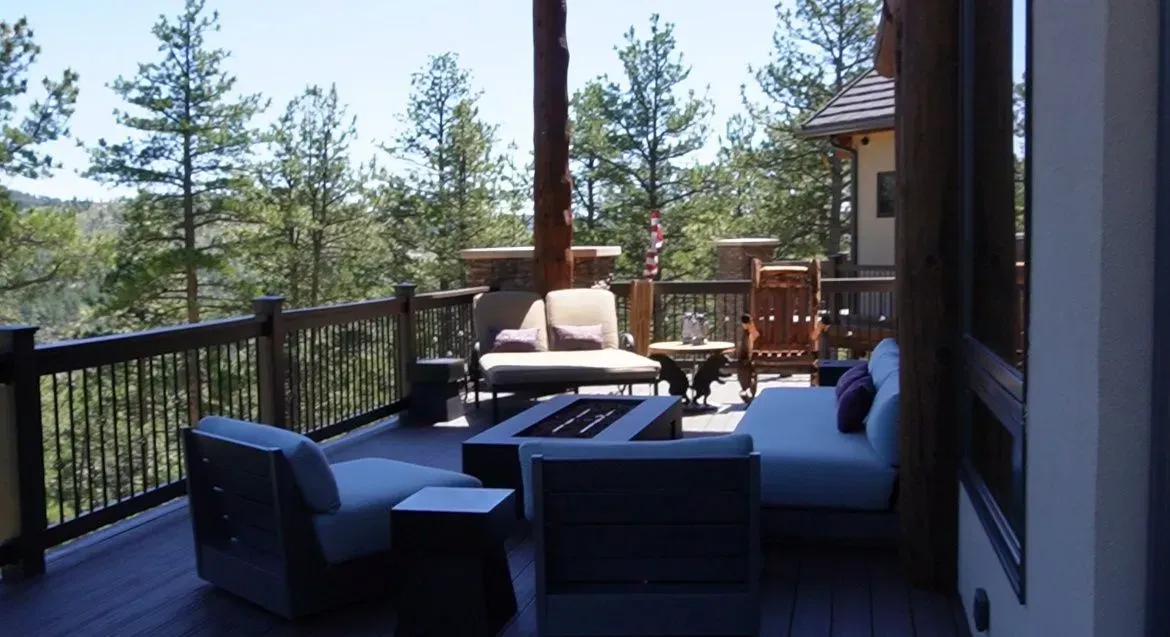 Outdoor deck with seating, fire pit, and forest view.