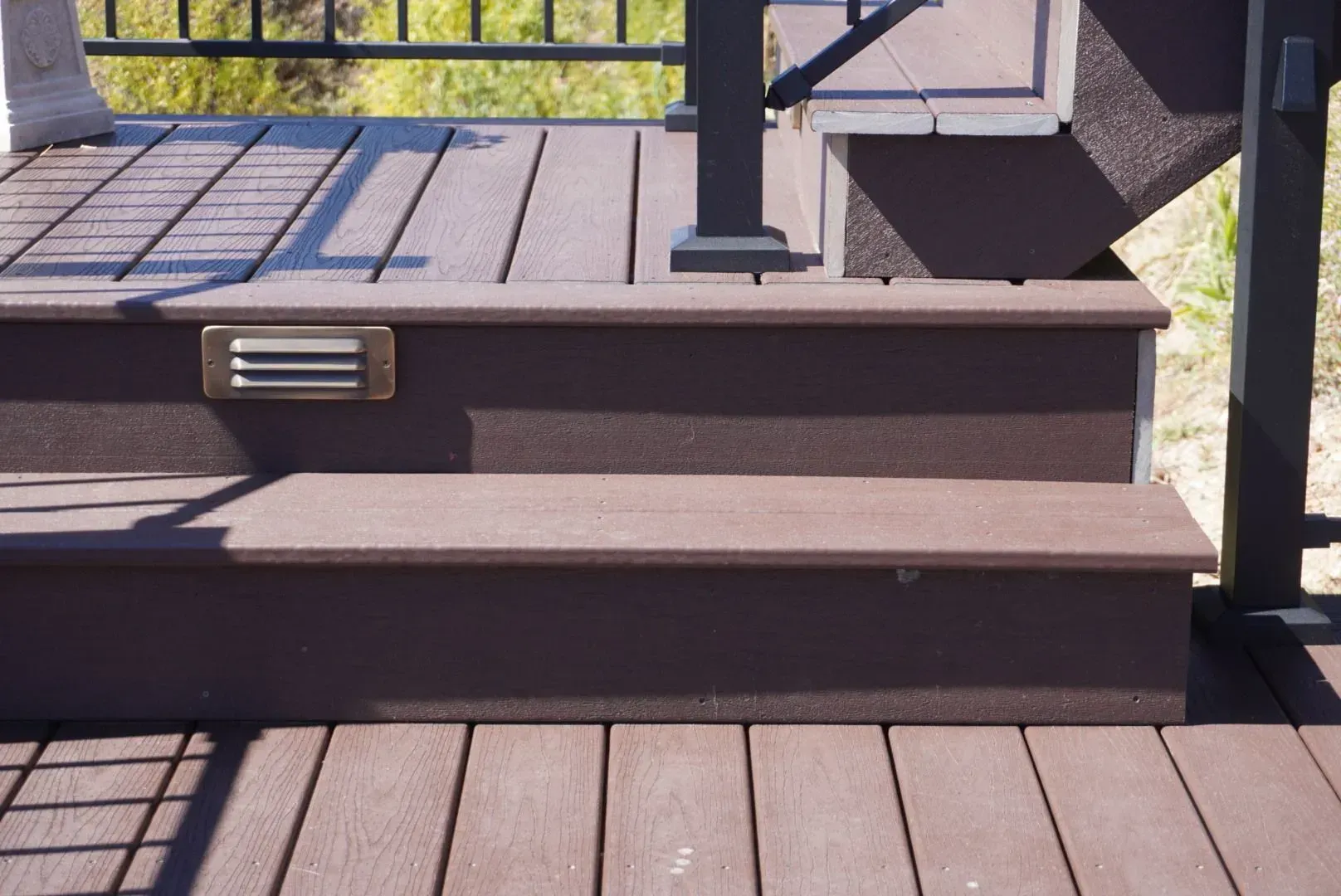 Dark brown composite deck with steps, a railing, and an inset light.