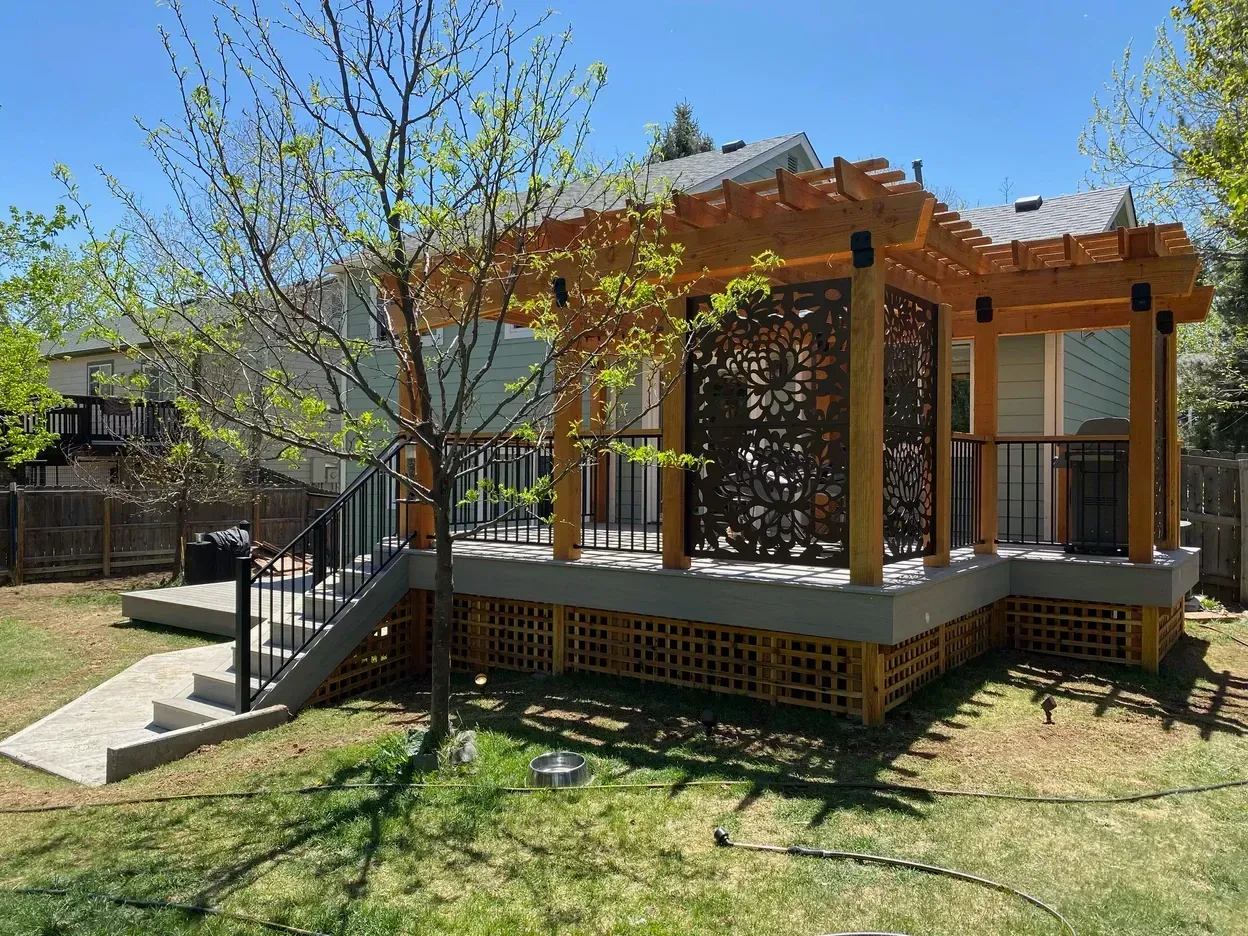 Backyard deck with pergola and decorative screen; brown wood, black railings, green grass.