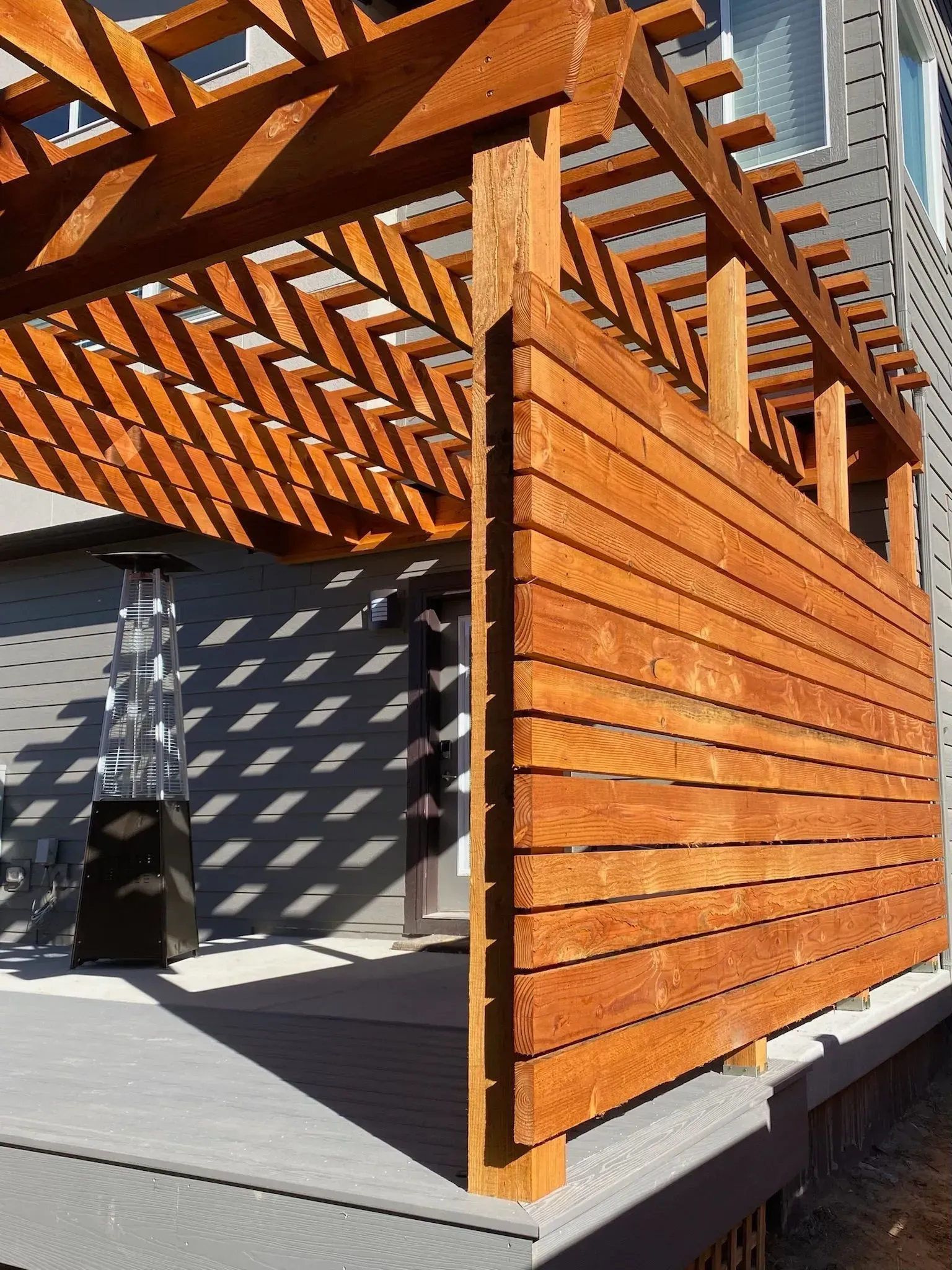Wooden pergola with slatted privacy screen on a deck. A patio heater is visible.