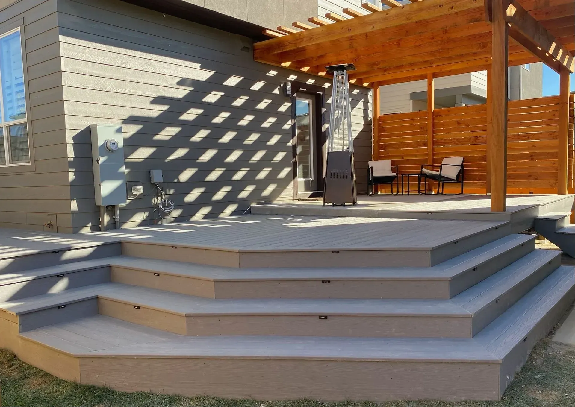 A multi-tiered deck with steps, pergola, and outdoor heater. Brown and tan tones.