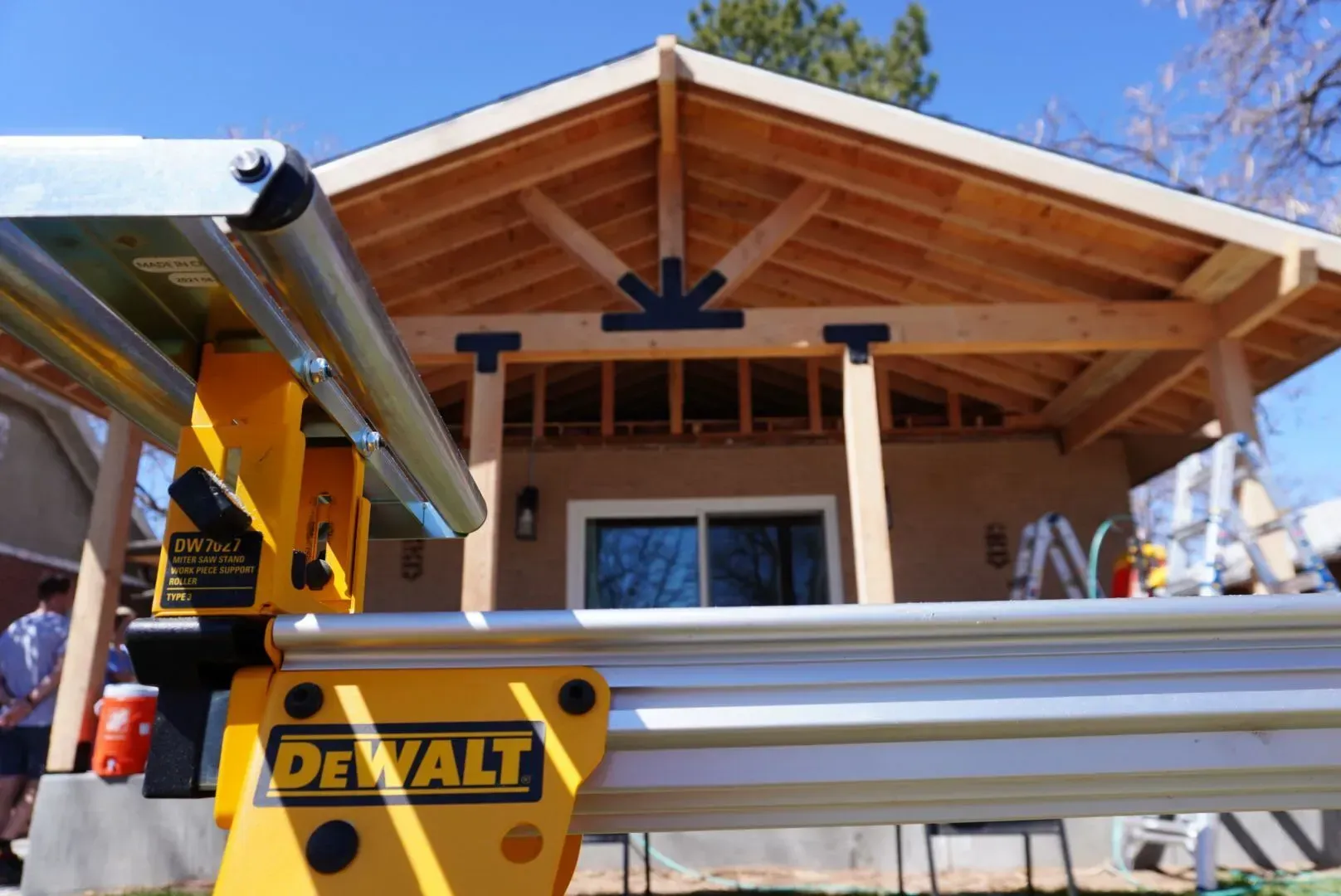 Yellow DeWalt saw in front of a new wooden patio with black brackets and a light brown stucco house.