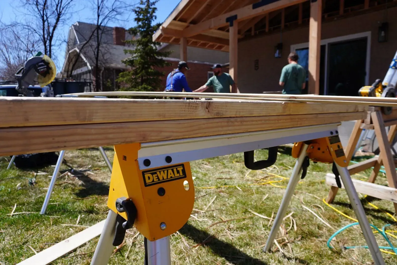 A yellow DeWalt miter saw with wood, and several men working on a construction project outdoors.