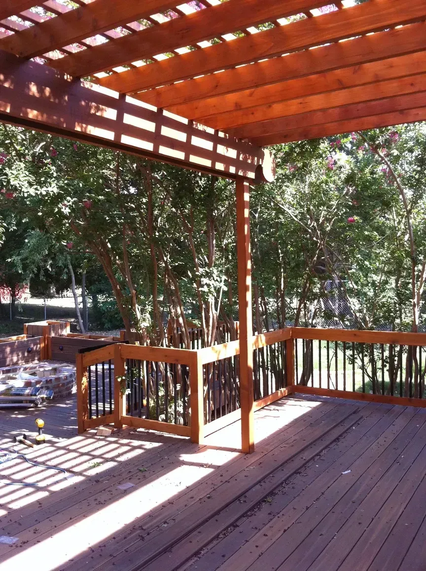Wooden deck with a pergola and black railing, surrounded by trees.