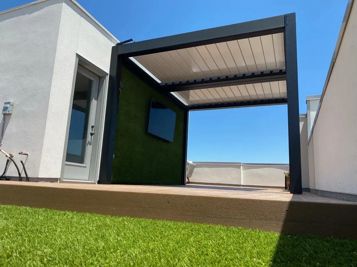 Pergola on a rooftop patio with green wall, blue sky, and artificial grass.