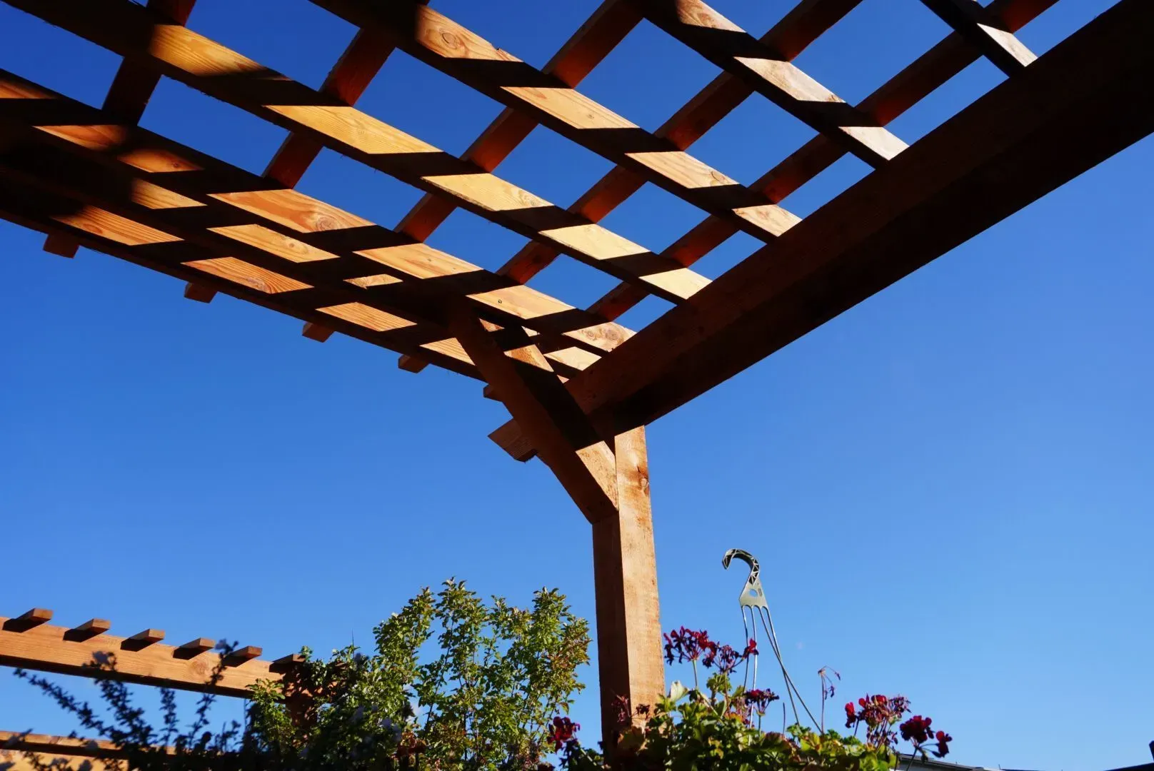Wooden pergola against a clear blue sky, casting shadows.