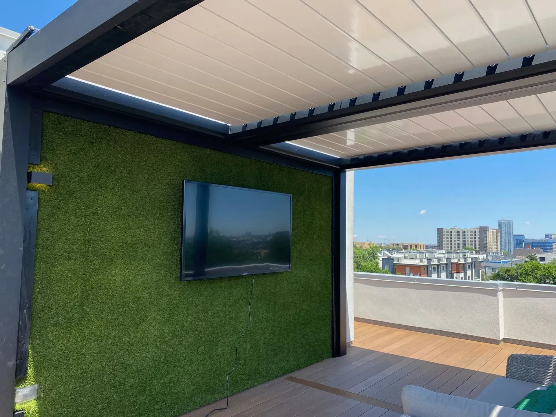 Outdoor space with TV on a green wall, under a white retractable roof, with cityscape view.