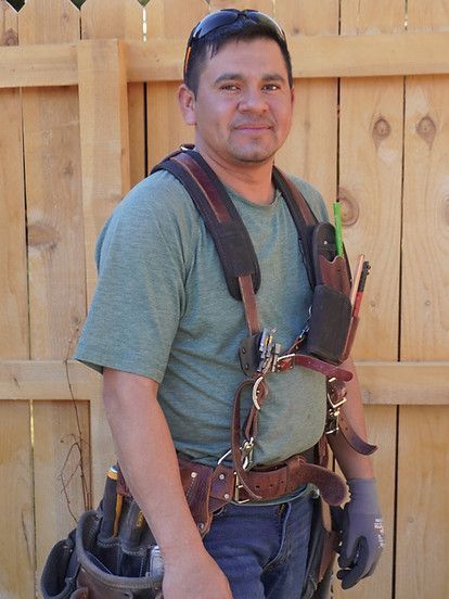 Man in work gear, smiling. Leaning against a wooden fence.