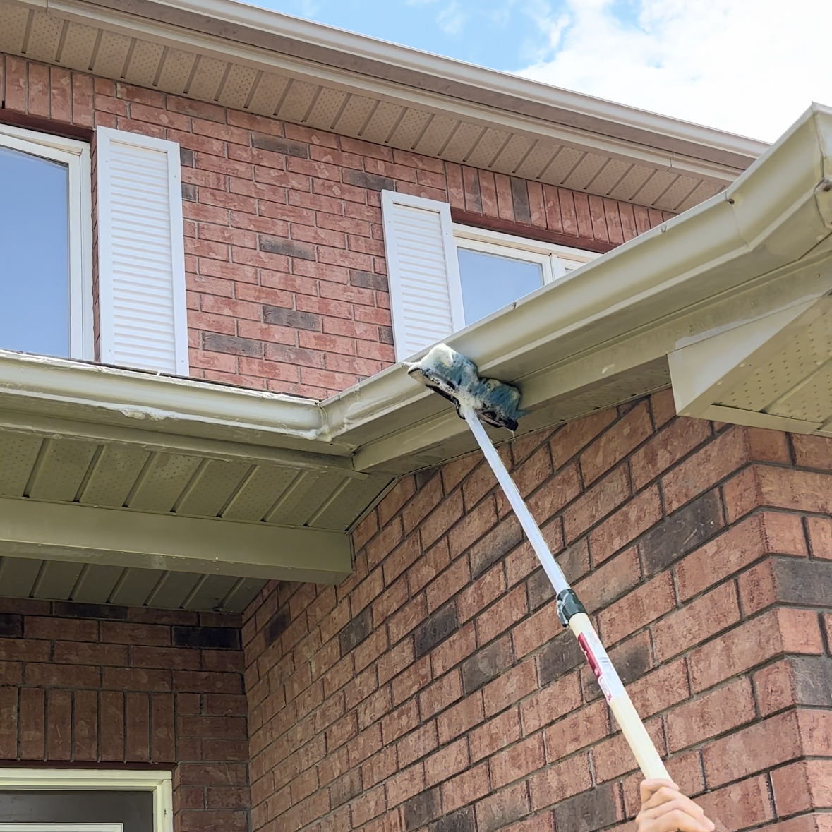 A person is cleaning the gutters of a brick house