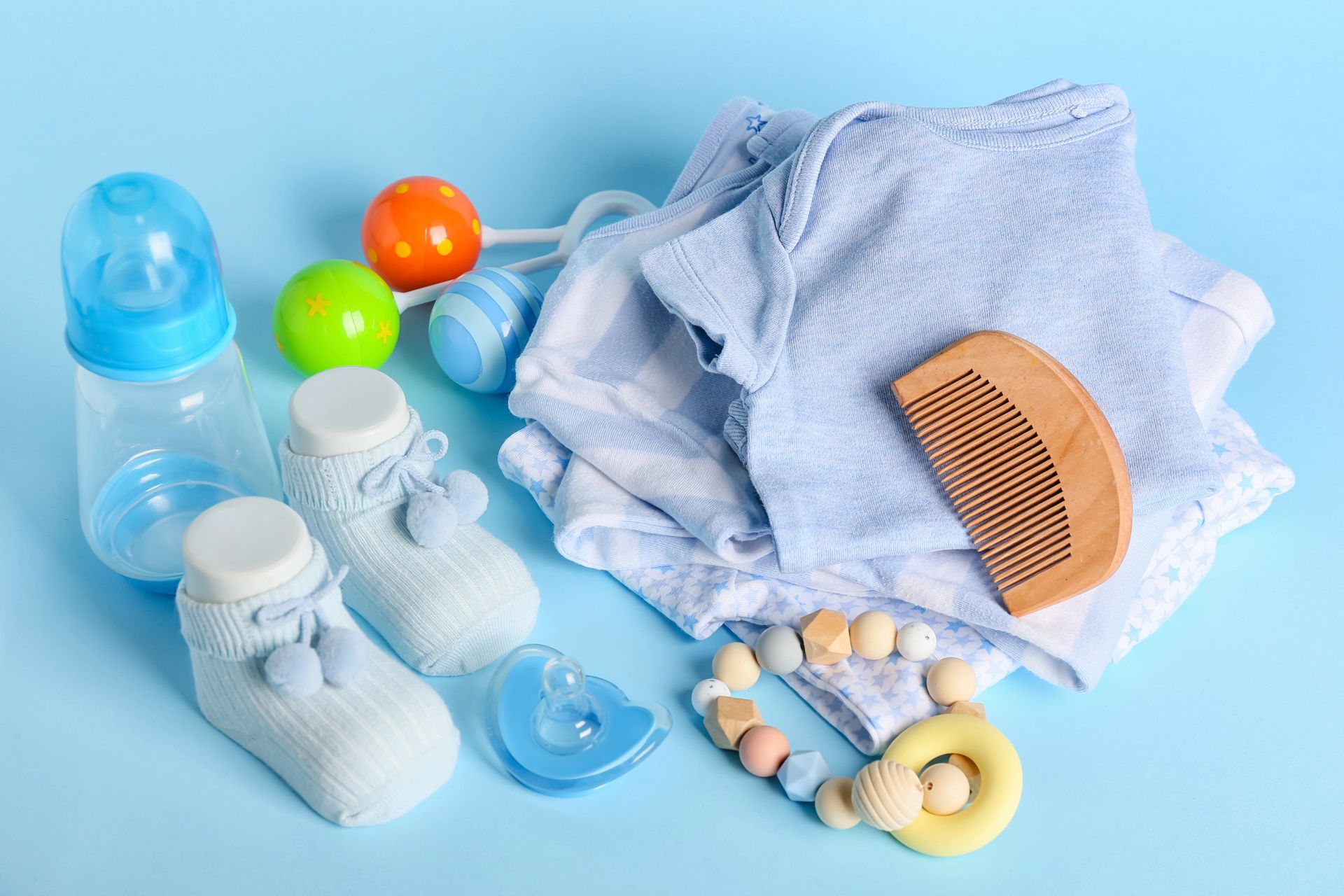 Articoli blu per neonati: biberon, vestiti, calzini, giocattoli, pettine e massaggiagengive su una superficie blu.