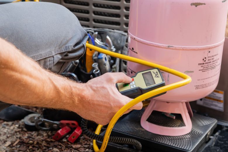 Person using a yellow gauge to check a pink refrigerant tank connected to an AC unit.