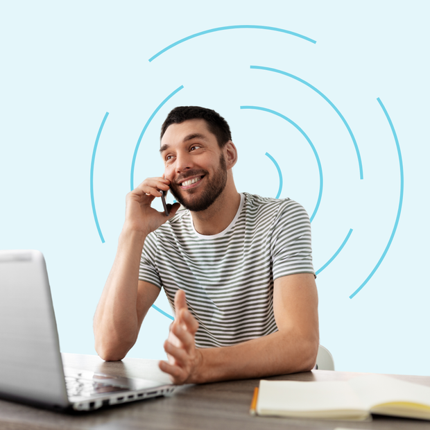 A man is sitting at a desk talking on a cell phone in front of a laptop.