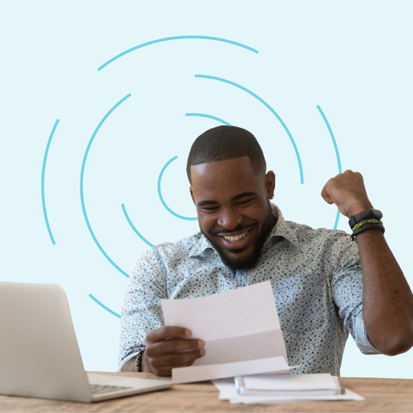 A man is holding a piece of paper in front of a laptop computer.