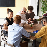 A group of people are sitting around a table with laptops.