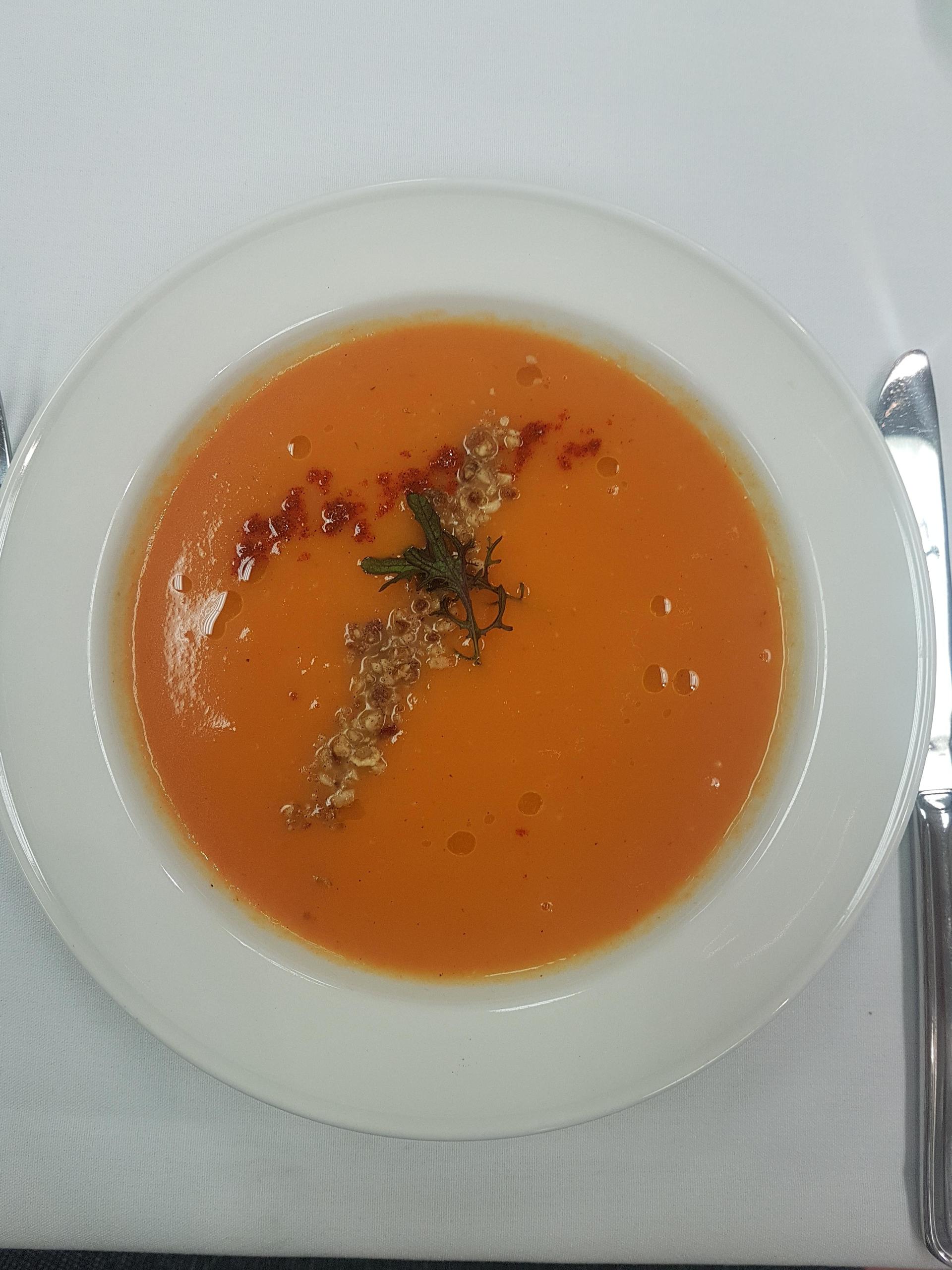 a white plate topped with a bowl of tomato soup on a table .