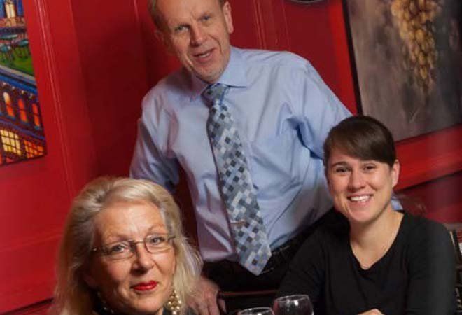 a man and two women are sitting at a table with glasses of wine .
