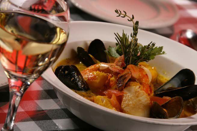 a bowl of seafood stew next to a glass of wine .