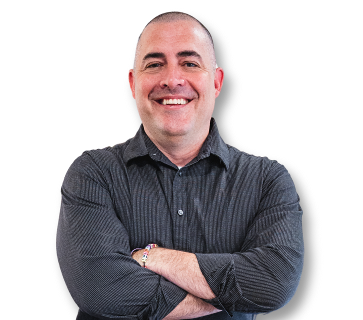 A man in a grey shirt is smiling while sitting in front of a laptop