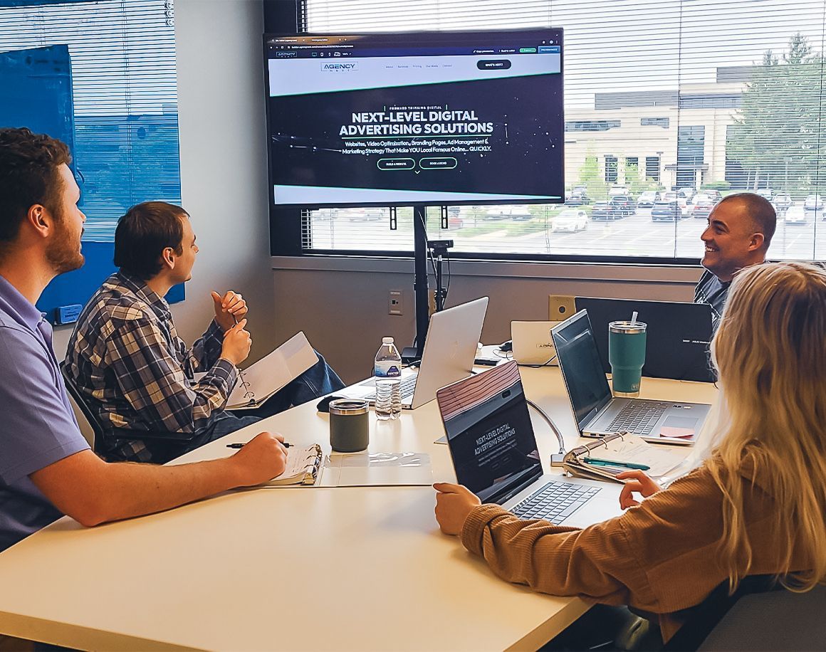 A group of people are sitting around a table with laptops.