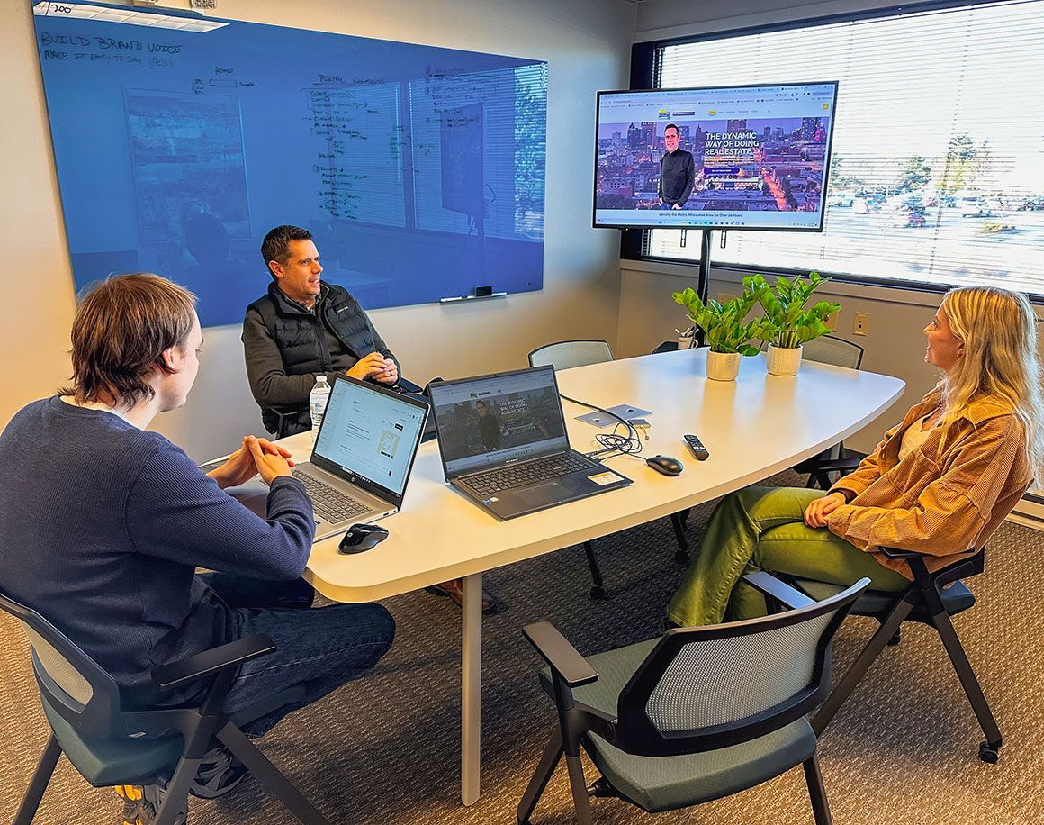 A group of people are sitting around a table with laptops in a conference room.