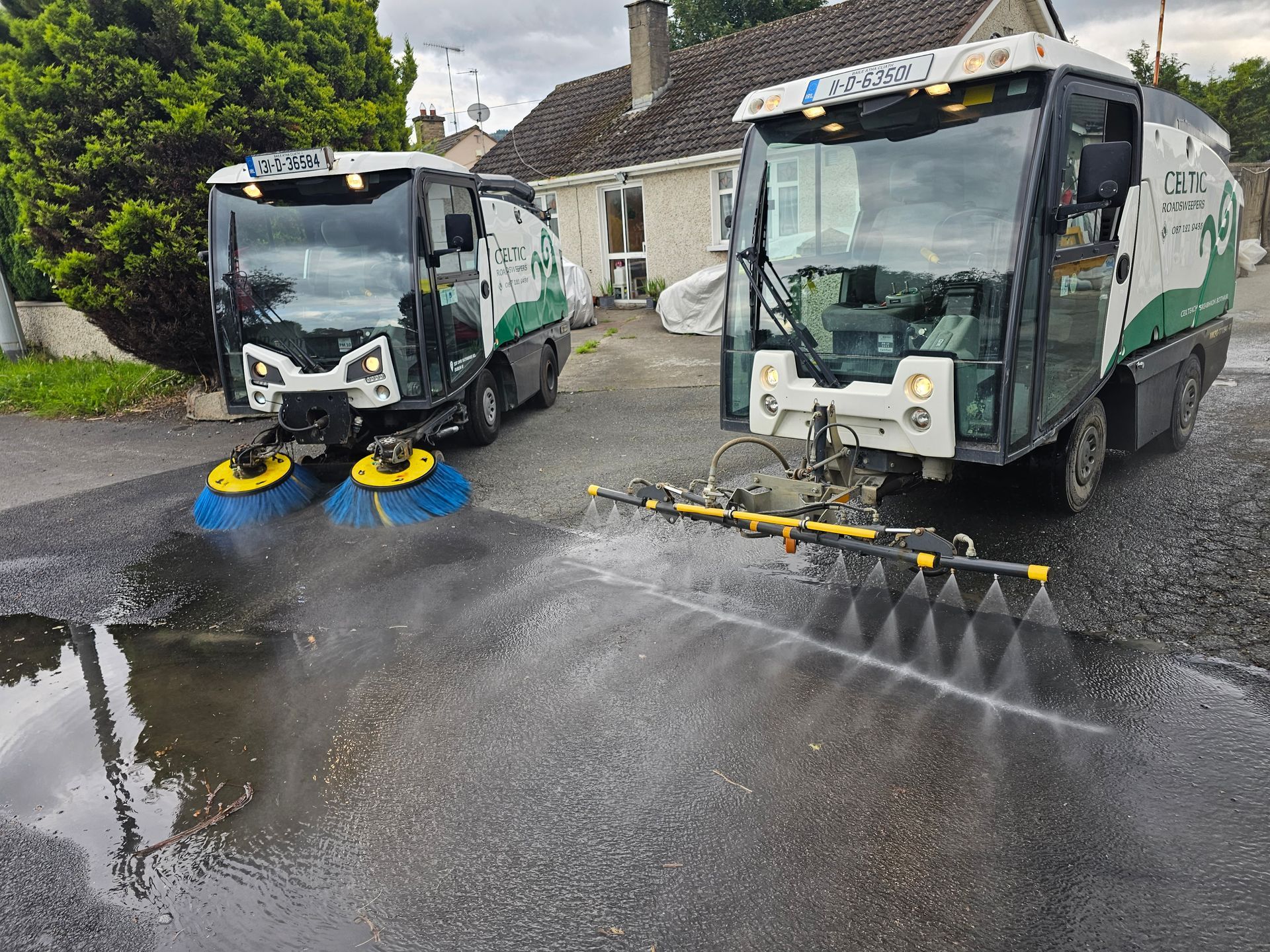 Two street sweepers are spraying water on a wet road.