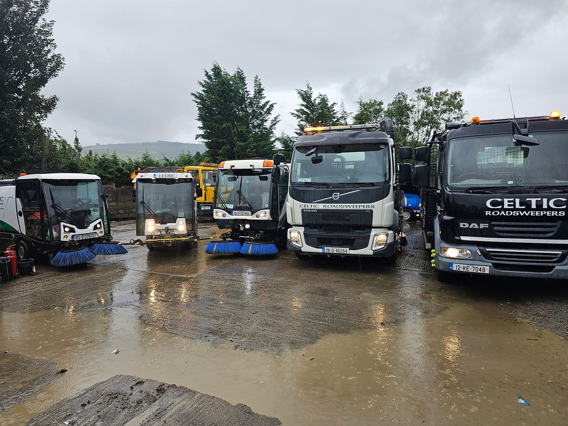 A group of celtic trucks are parked in a muddy lot