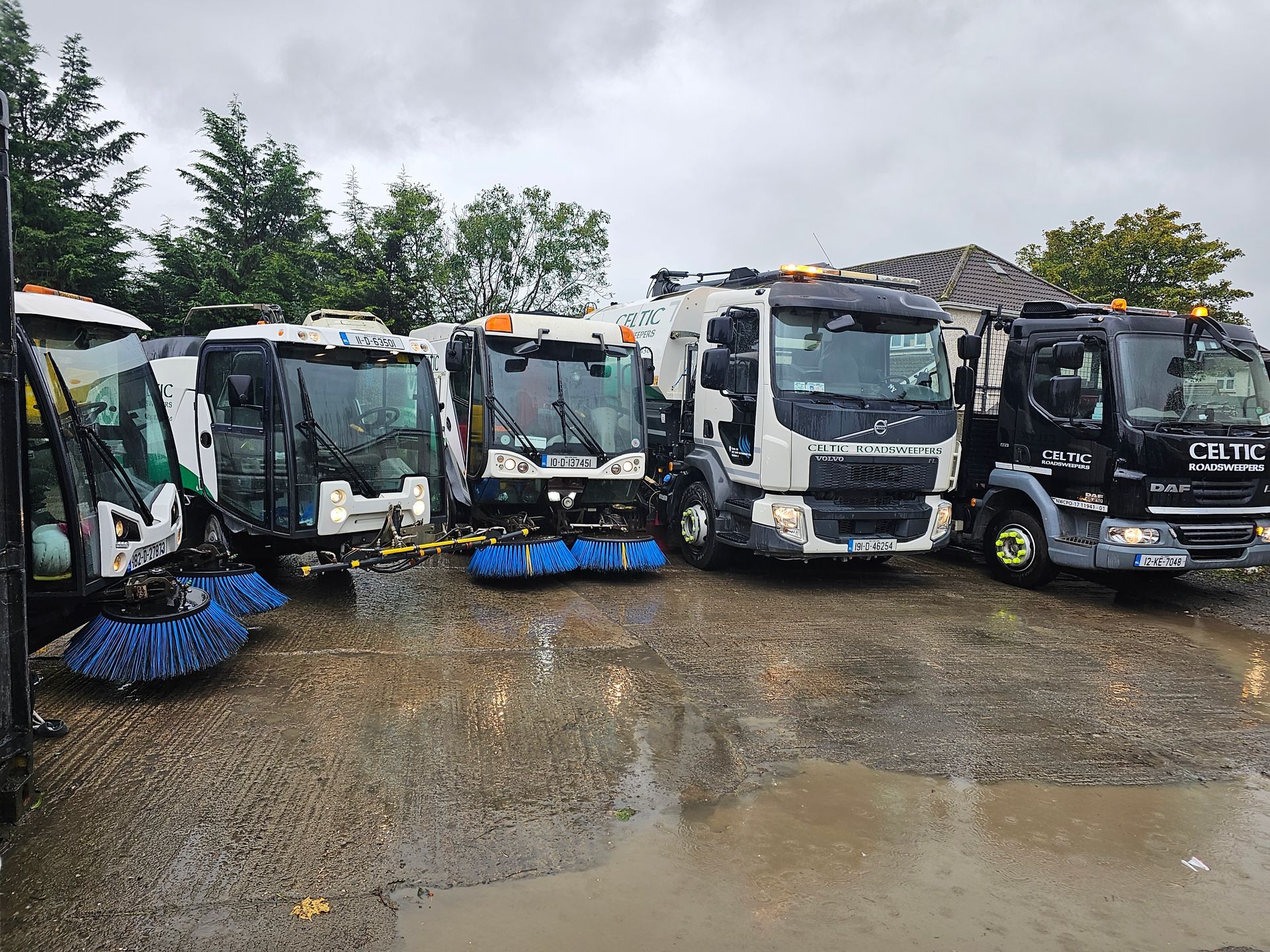 A row of trucks parked in a parking lot on a rainy day.