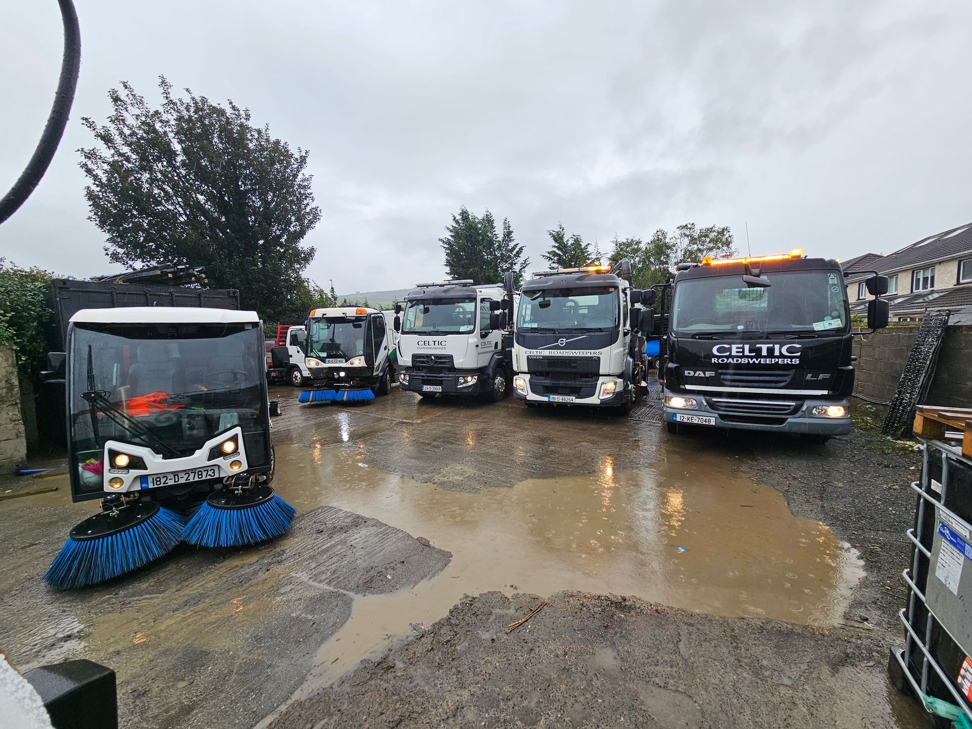 A row of trucks are parked in a muddy lot on a rainy day.