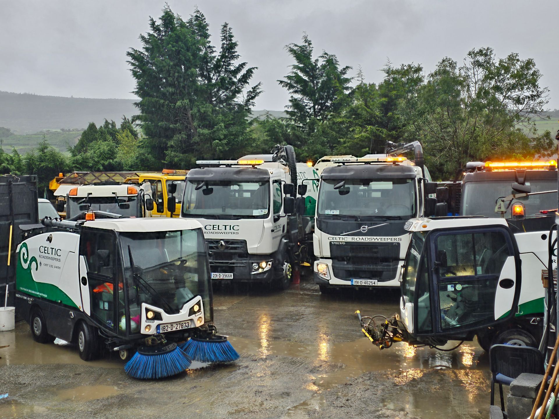 A row of street sweepers are parked in a parking lot