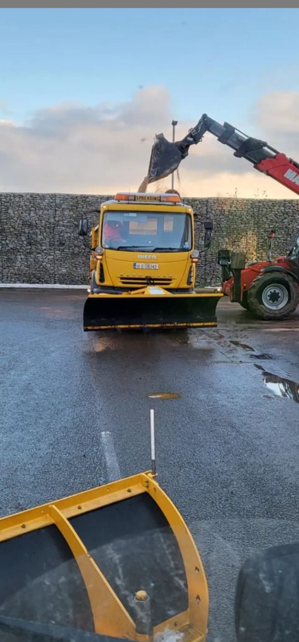 A yellow truck is driving down a wet road next to a red tractor.