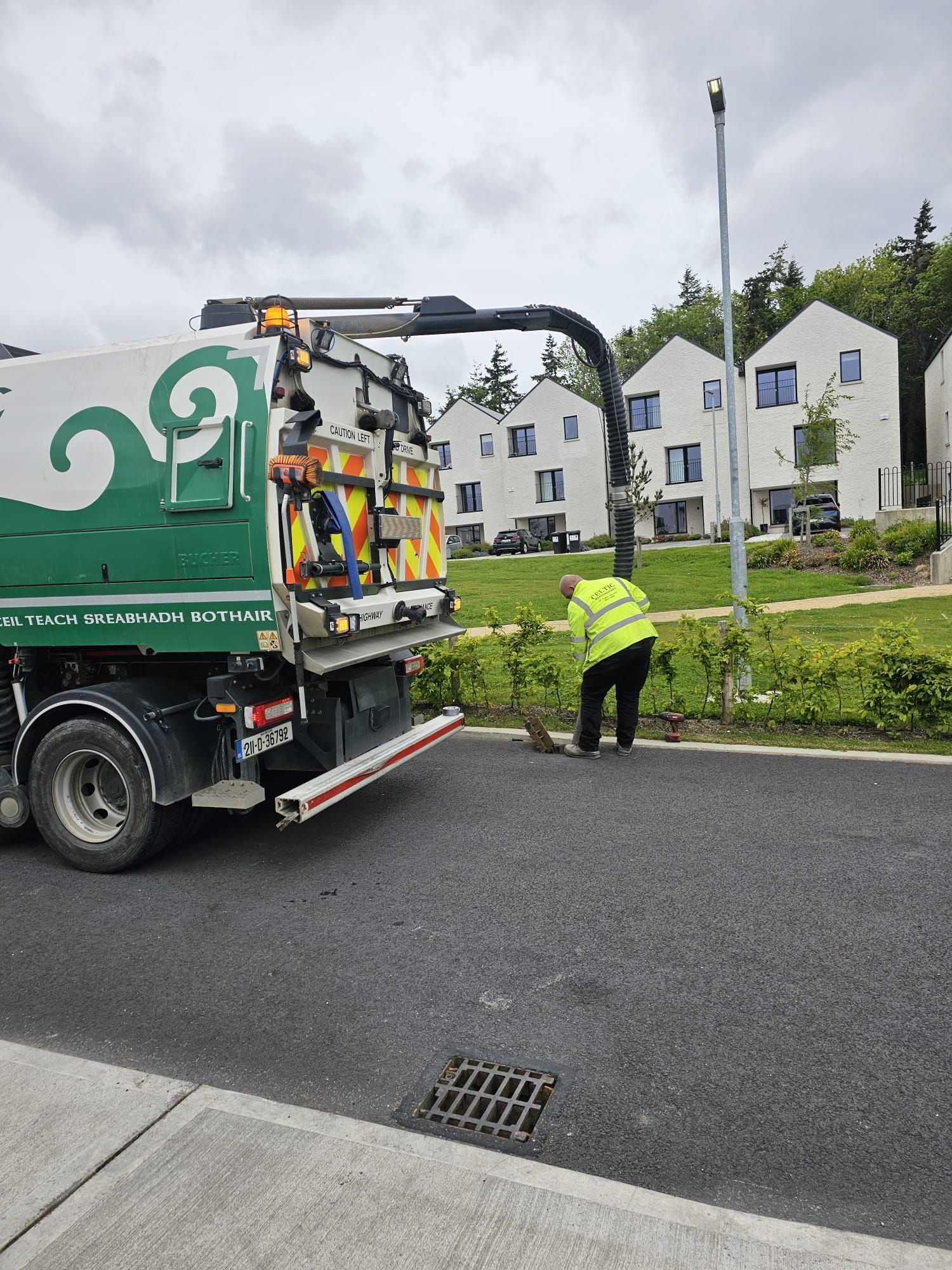 A man is standing next to a garbage truck on the side of the road.
