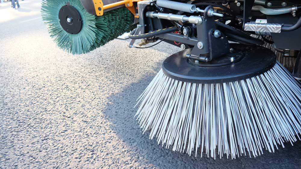 A street sweeper is cleaning the road with brushes.