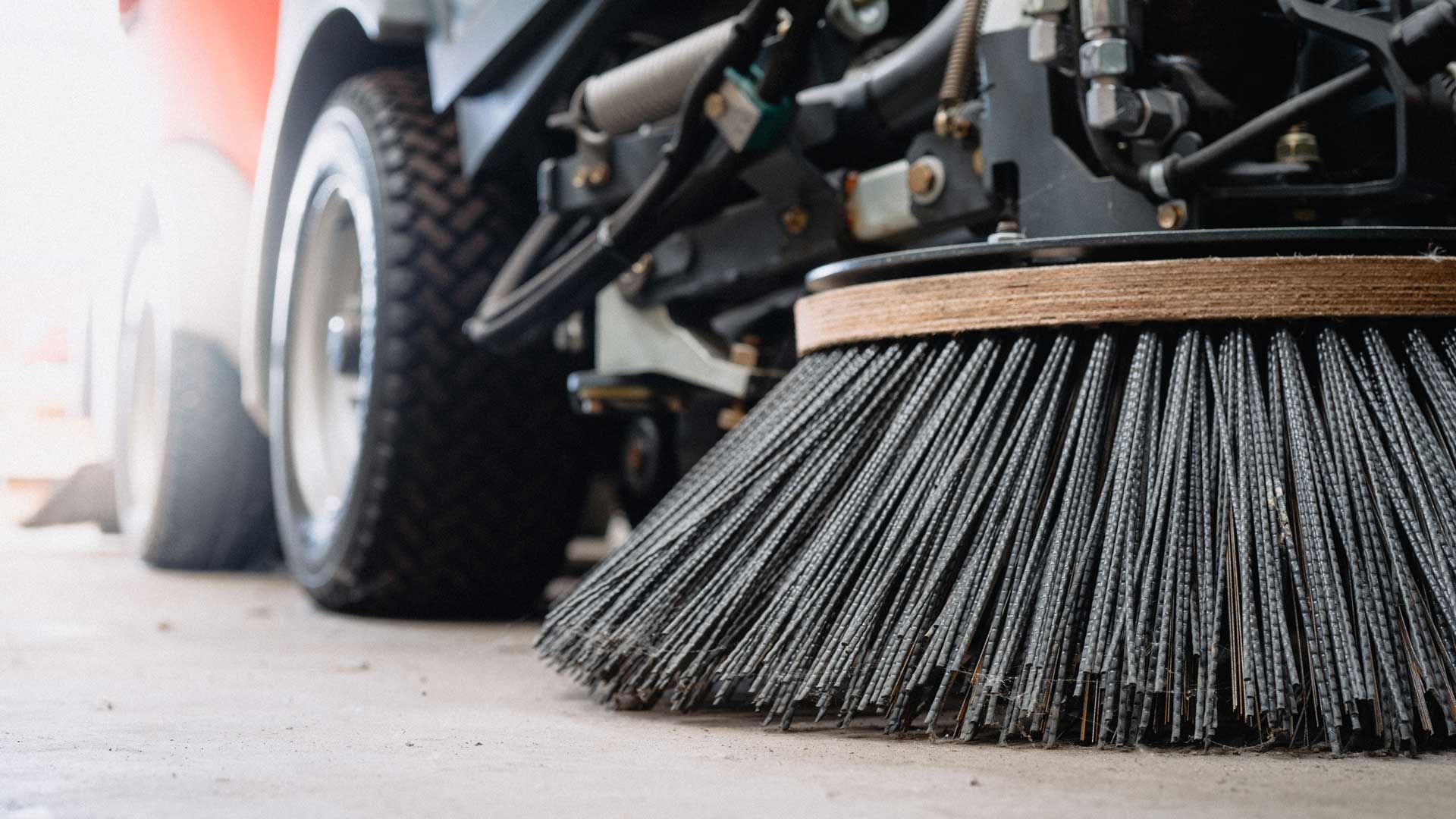 A street sweeper is cleaning the ground next to a car.