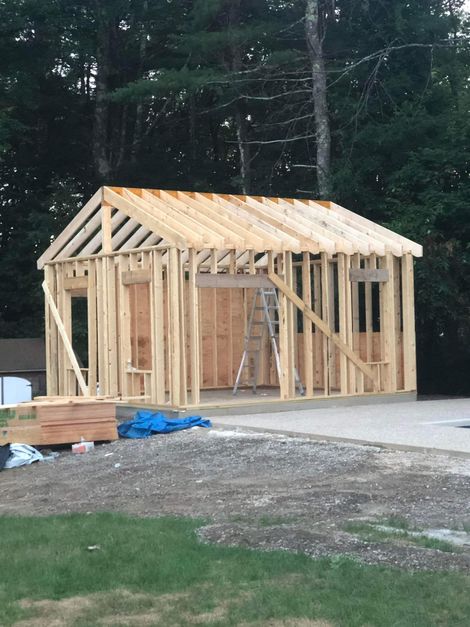 Wooden building frame under construction; includes windows, door, and ladder, on a gravel base.