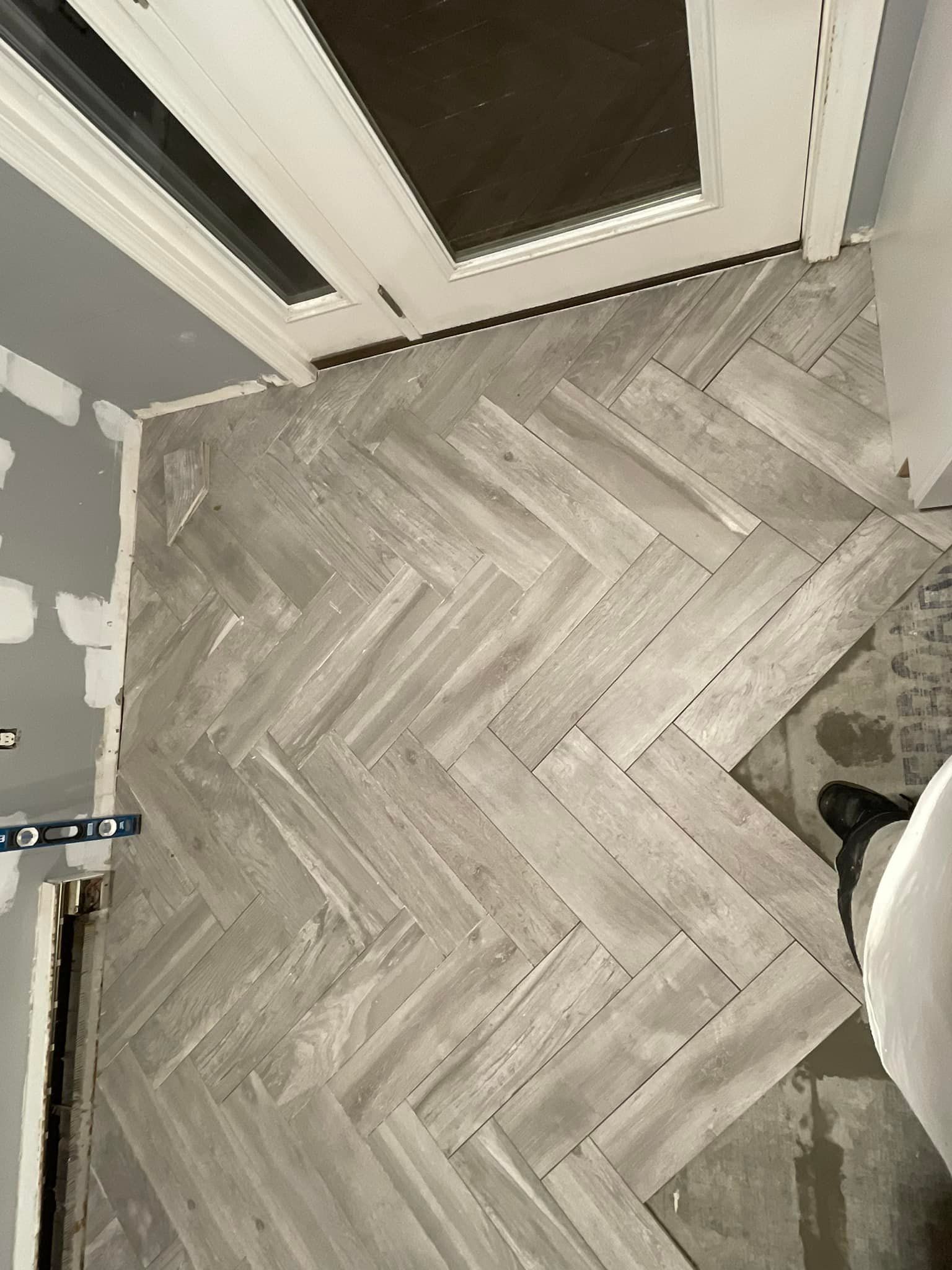 Herringbone pattern floor tiling. Gray-toned tiles laid near a doorframe.