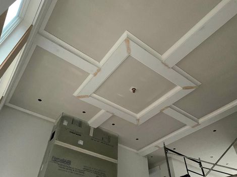 Ceiling with recessed squares and beams under construction in a room with a fireplace.