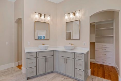 A spacious bathroom with dual sinks, gray cabinets, gold fixtures, and a walk-in closet.