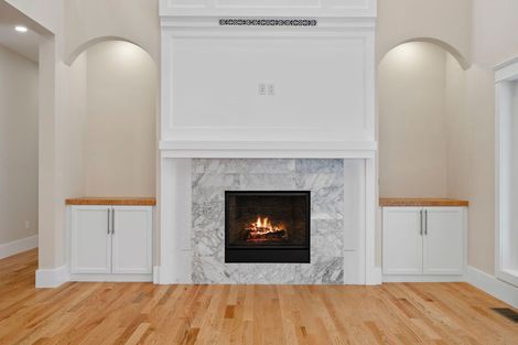 Fireplace with marble surround, flanked by white cabinets and arches in a light-colored room with wood flooring.