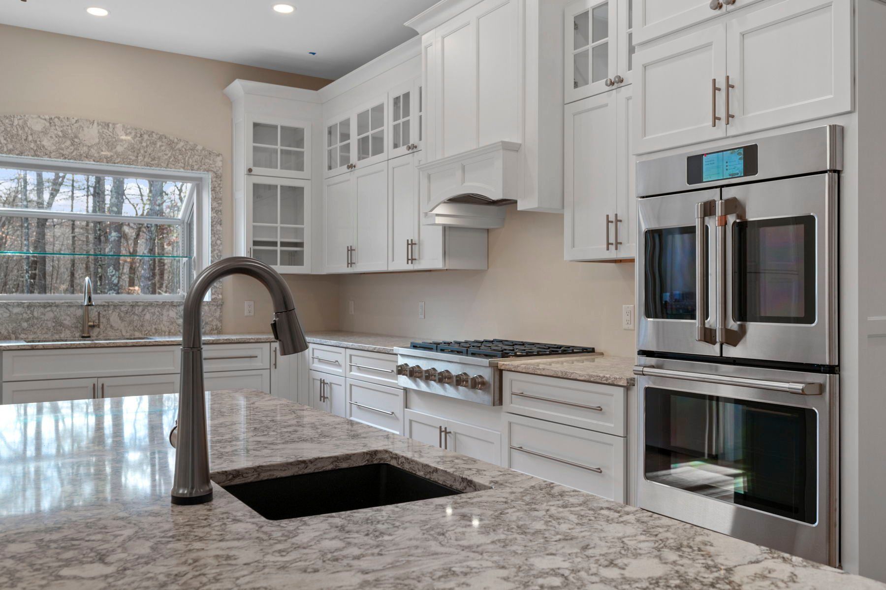 Modern white kitchen with granite countertops, stainless steel appliances, and dark faucet.