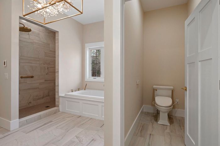 Bathroom with shower, tub, and toilet; marble-look tile, beige walls, natural light.