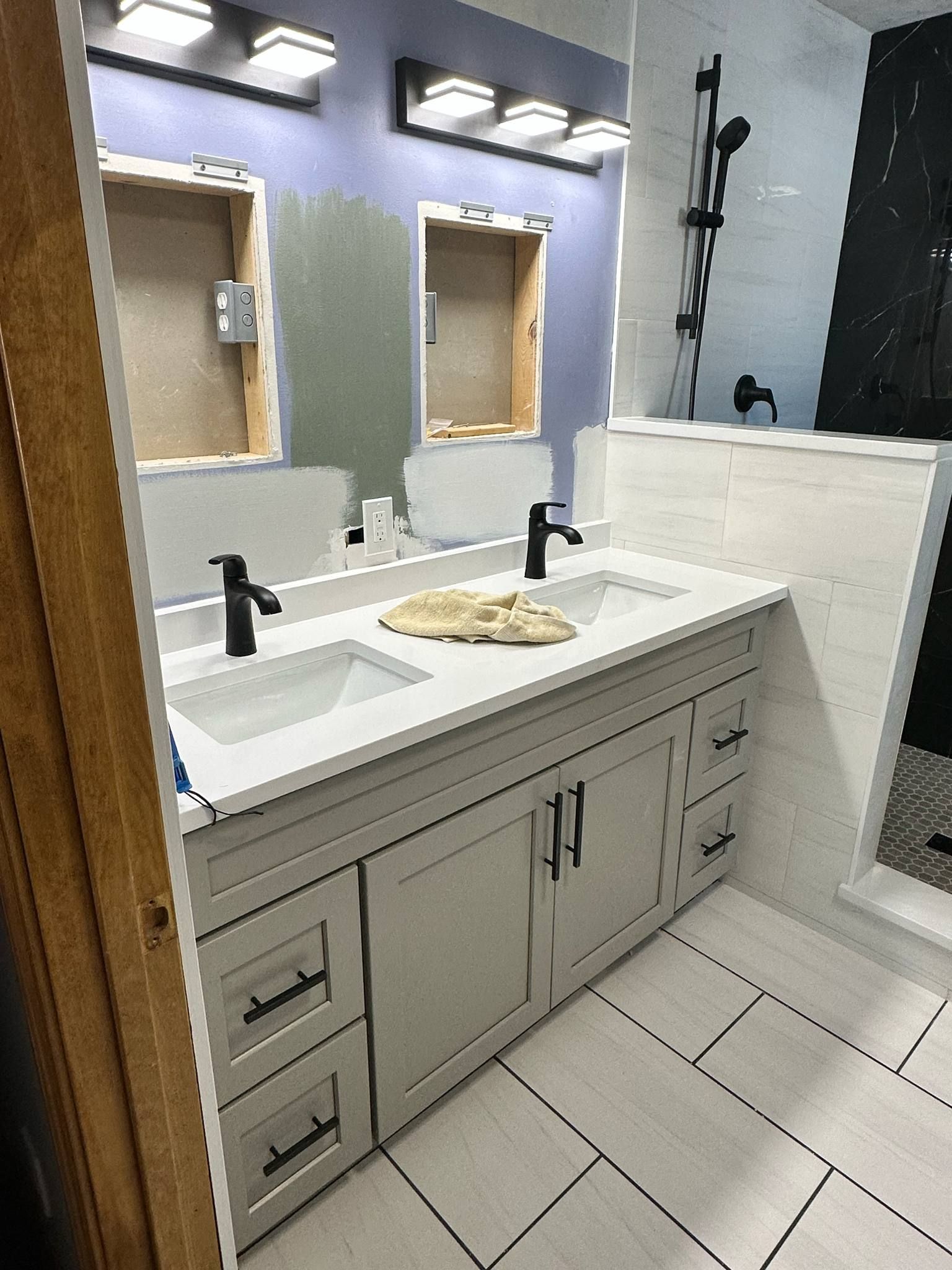 Bathroom renovation: double vanity with black fixtures and light gray cabinets; white tile floor and walls.