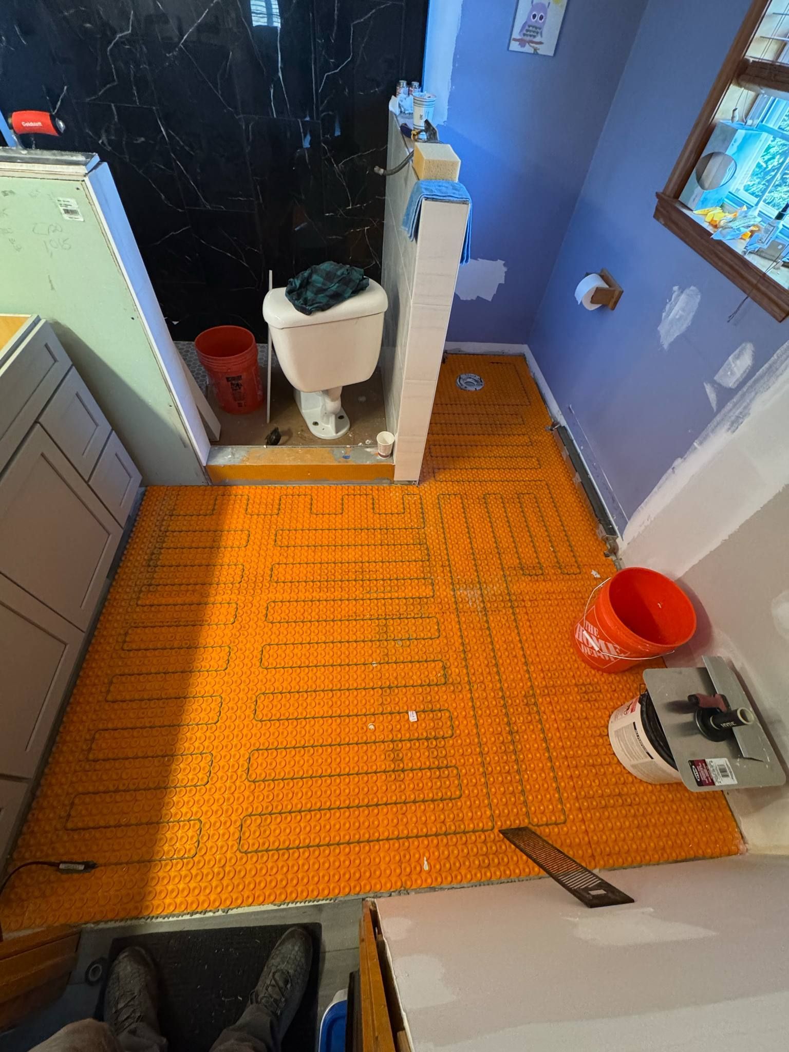 Bathroom under renovation with orange tiling, toilet, and buckets.