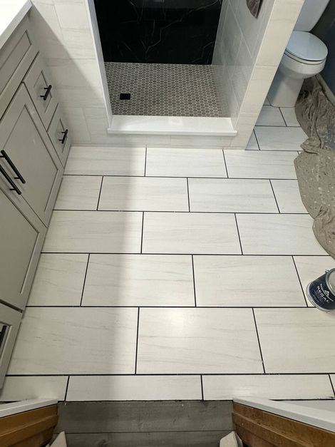 Bathroom with tiled floor, shower, and toilet. Light gray rectangular tiles with black grout.