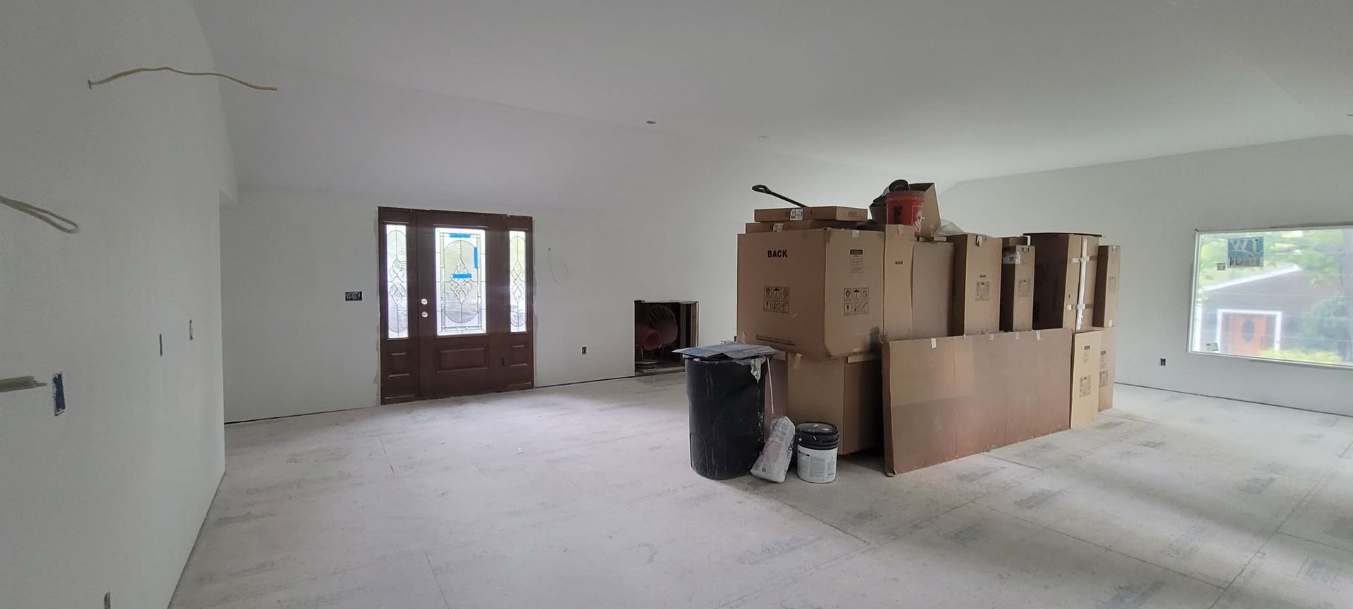 An empty room with bare floors, boxes, a door, and a window.