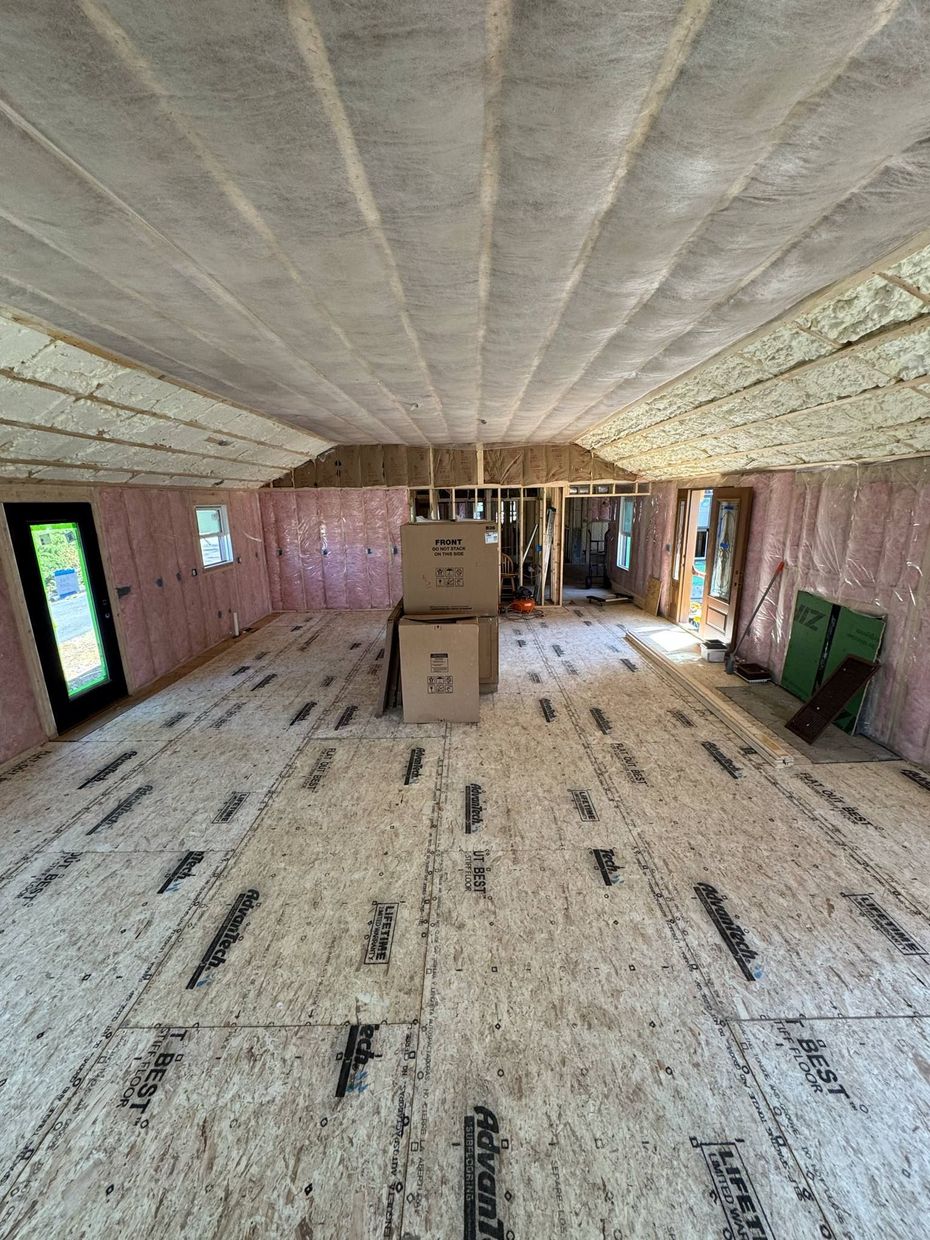 Interior of a room under construction: insulated pink walls, wood flooring and ceiling, cardboard boxes in center.