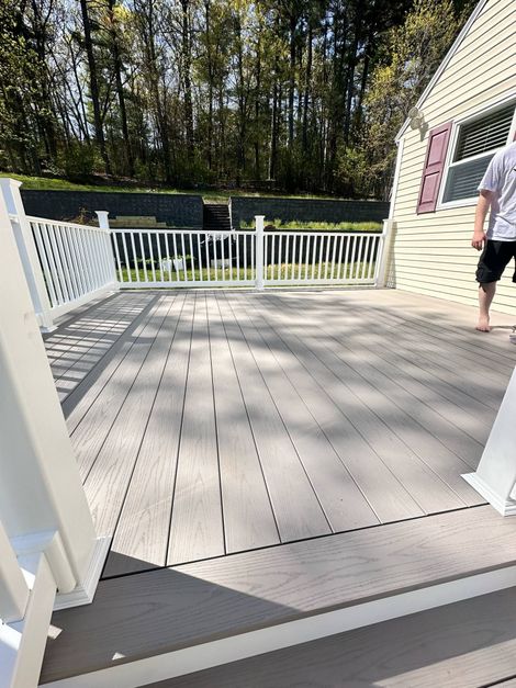 A spacious deck with a white fence and railing, person standing. Background trees and building.