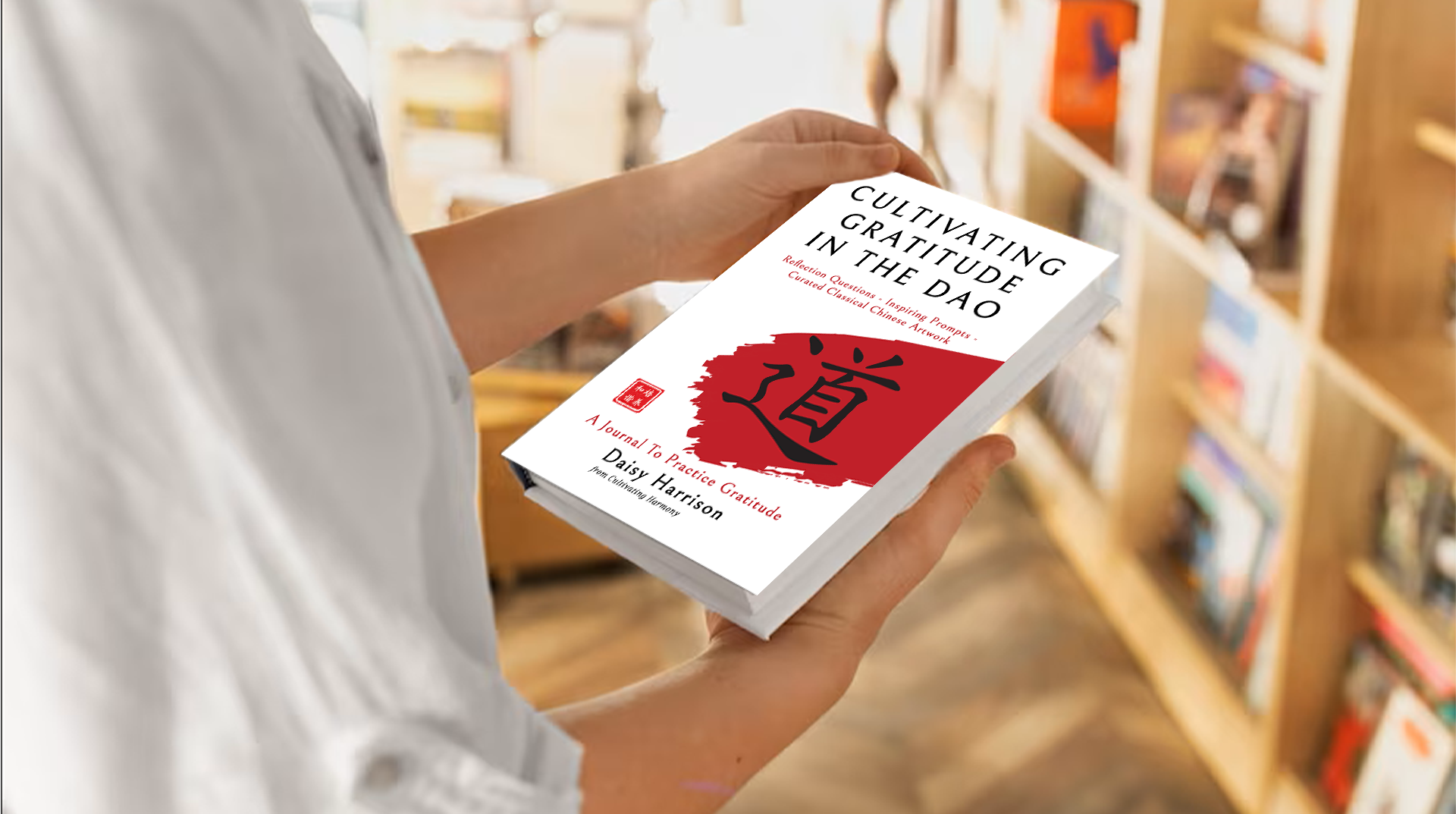 Person in a library holding the book “Cultivating Gratitude In The Dao” by Daisy Harrison and looking at the cover.