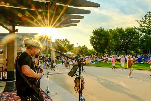 Musician performing at Birmingham's Shain Park concert series while families sit on the grass and enjoy live music